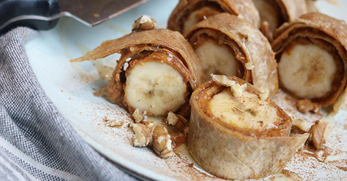 Bananen-Wraps mit Erdnussbutter und Walnüssen auf hellblauem Teller.