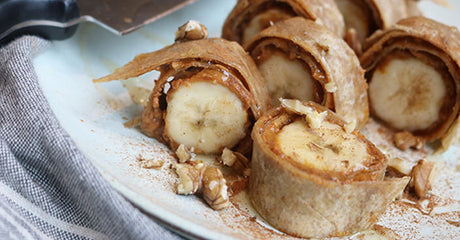 Bananen-Wraps mit Erdnussbutter und Walnüssen auf hellblauem Teller.