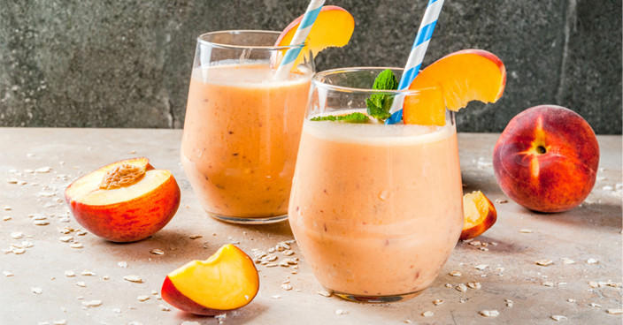 Deux smoothies à la pêche avec pailles et morceaux de fruits.