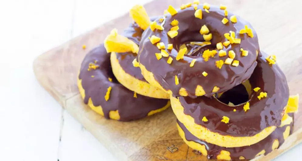 Three healthy protein donuts with chocolate glaze and orange zest on wooden board.