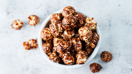 Chocolade popcorn in witte kom op lichte achtergrond.