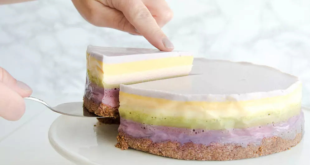 Bunter Schichtkuchen mit violetter, grüner, gelber und weißer Creme auf weißem Teller.