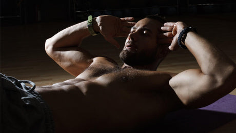 Shirtless man doing crunches on yoga mat in dark gym.