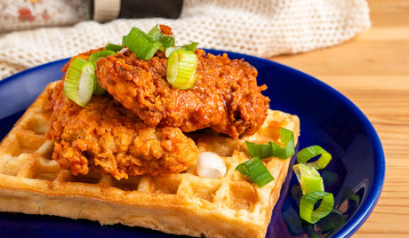 Wafel met krokante kip en lente-ui op blauw bord.