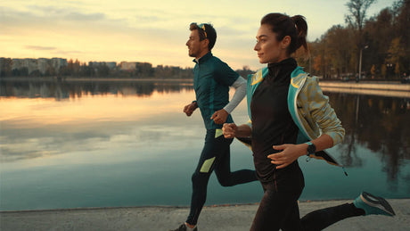 Couple running outdoors by water during sunrise.