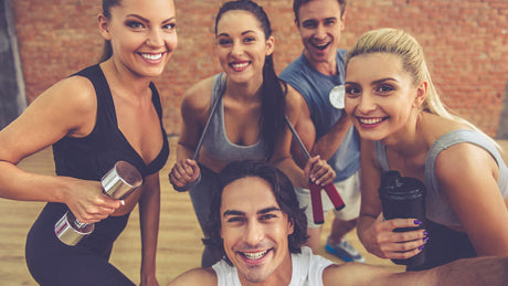 Happy fitness group posing with dumbbells and shaker bottles in studio.