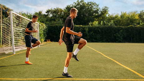 Voetballers doen warming-up op kunstgrasveld bij doel.