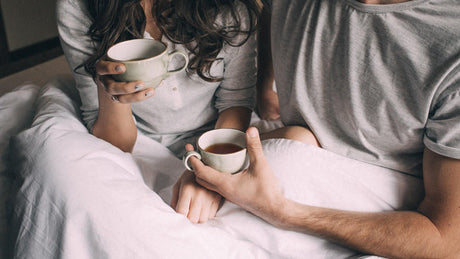 Couple assis au lit buvant des tasses de thé.