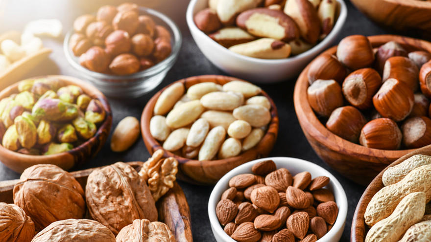 Assortiment ongebrande noten in houten en glazen schaaltjes.