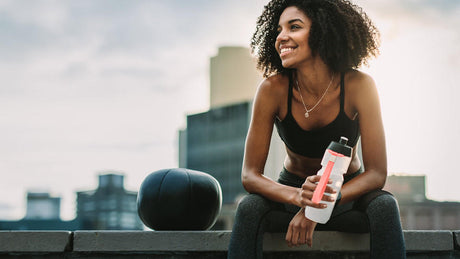 Sportlerin mit Trinkflasche entspannt nach Workout auf Dach.