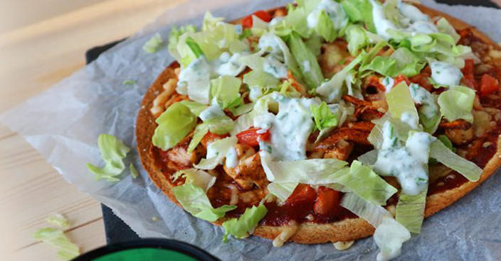 Pizza garnie de légumes, salade et sauce blanche.